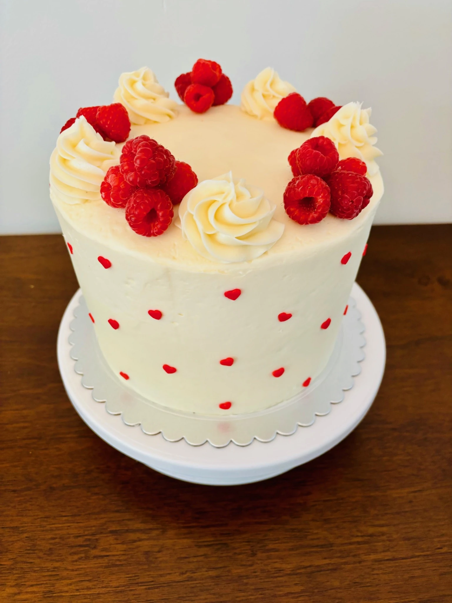 White buttercream raspberry cake with red hearts, fresh raspberries, and piped frosting made by Texas Rose Cakeries